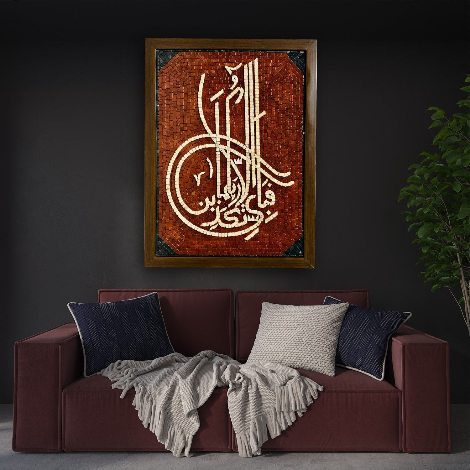 A handcrafted Islamic wall art featuring the word 'Fabiallah' in red and black stones, displayed above a dark sofa with a gray blanket and multicolored cushions.