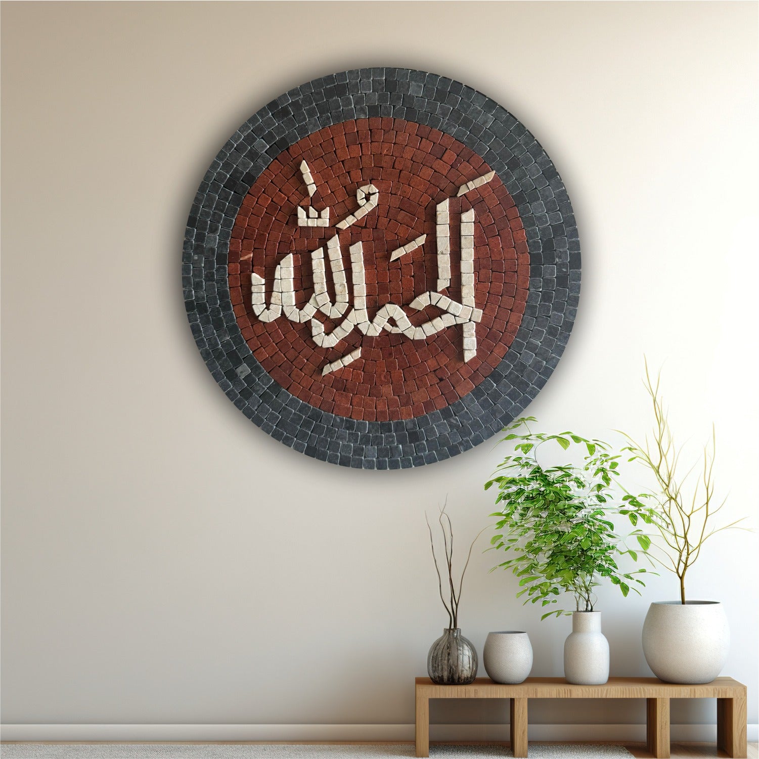 A round 'Alhumdulilah' Islamic calligraphy art piece in black and red stone mosaic, displayed on a wall above a wooden bench with a green plant.