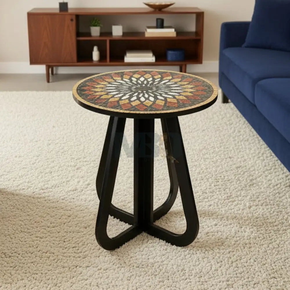 A mosaic accent coffee table with an infinity loop base and a geometric patterned top, placed on a tiled floor next to a potted plant and a brick wall.