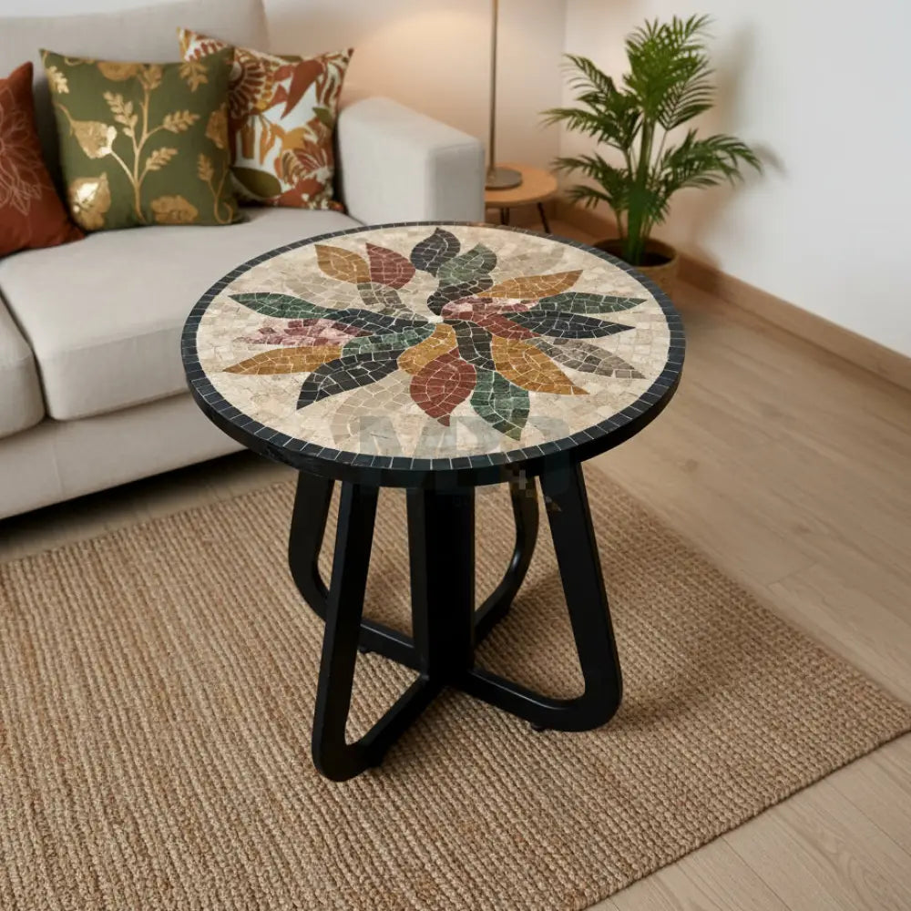 A round mosaic coffee table with a floral pattern and a black metal infinity loop base, placed on a tiled floor next to a potted plant.